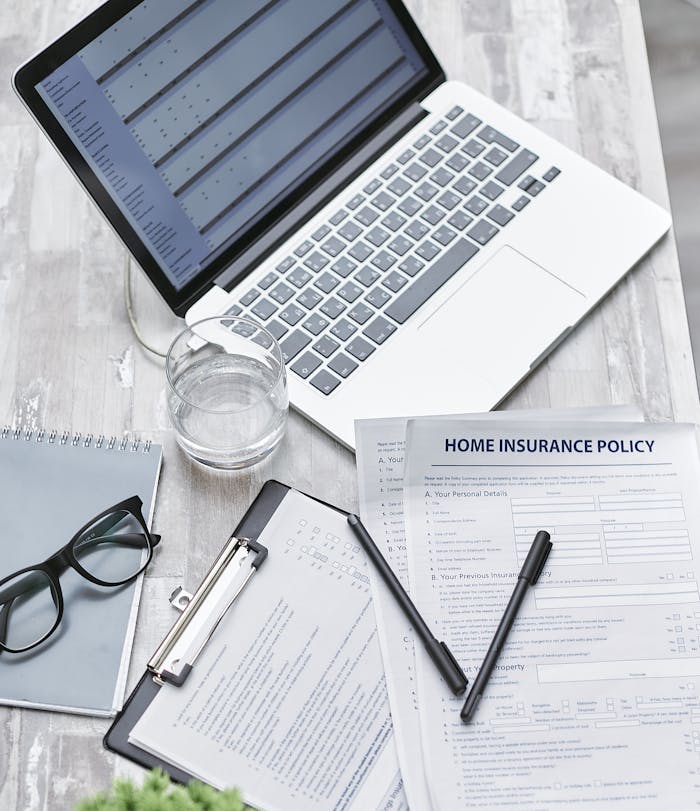 Top view of a desk with laptop, insurance forms, and office supplies, ideal for business or finance topics.